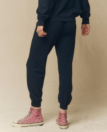 A person wearing The Cropped Sweatpant in True Navy by THE GREAT. FALL 23 KNITS, a matching hoodie, and pink high-top sneakers with star designs stands against a plain backdrop, not facing the camera.