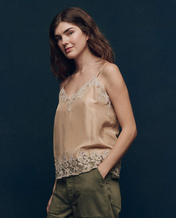 Against a dark background, a person wears The Legacy Top in Nude by THE GREAT. SP25 COLLECTORS and green pants, epitomizing effortless fashion apparel elegance.