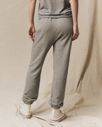 Person wearing The Stadium Sweatpant in Varsity Grey by THE GREAT. CORE KNITS with an elasticated waist and white sneakers, standing with their back to the camera against a beige backdrop.