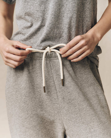 Close-up of a person adjusting the white drawstring on a pair of "The Stadium Sweatpant" in Varsity Grey by THE GREAT. CORE KNITS, wearing a matching grey t-shirt.