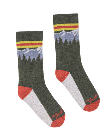 Introducing The Ridge Runner Sock in Evergreen by THE GREAT. FALL 23 TGO – a pair of green socks adorned with a mountain and tree pattern near the top, featuring red toes and heels, and white soles. Crafted from luxurious merino wool for your everyday adventure.