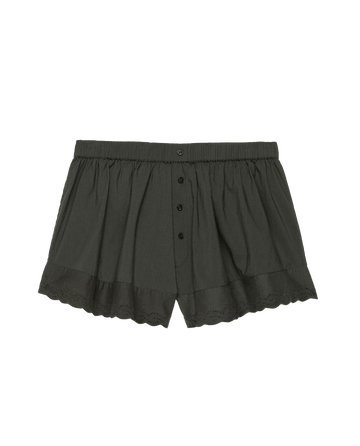 The Eyelet Tap Short by THE GREAT. PS25 SLEEP features a button front, elastic waistband, and scalloped Victorian-inspired eyelet lace trim on a plain black background, crafted from soft cotton voile.