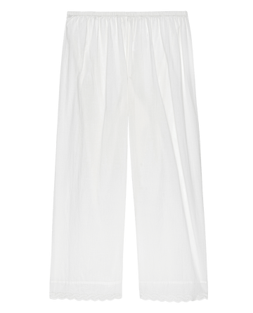The Eyelet Easy Sleep Pant in True White by THE GREAT. PS25 SLEEP is a pair of white, wide-legged pants crafted from cotton voile fabric with an elastic waistband and scalloped hems adorned with delicate eyelet lace trim.