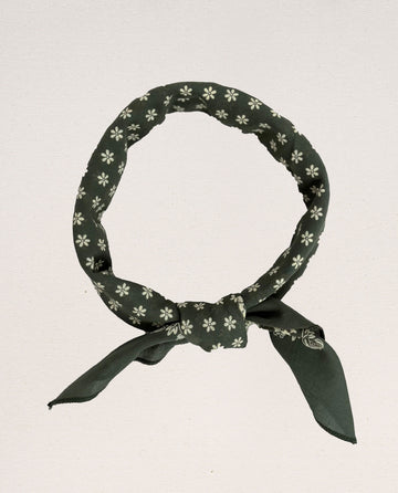The Bandana -- Small -- Army Green by THE GREAT. SP24 D2 features a white floral pattern and is tied into a circular shape with a knot at the bottom, evoking vintage handkerchief aesthetics. Made from 100% cotton, it offers an ultra-soft feel.