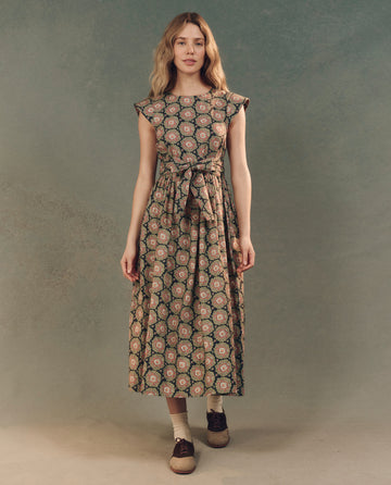 A person poses against a mottled backdrop in The Tulsa Dress by THE GREAT. SP25 D2, showcasing the Heirloom Paisley pattern and a chic belt.