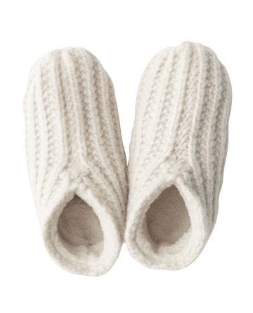 A pair of cream Bootie Slippers by THE GREAT. HOL 24 SLEEP, featuring a textured wool exterior and cozy sherpa lining with an open heel design, arranged side by side and viewed from above—ideal as a holiday gift.