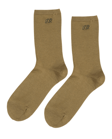 A pair of THE GREAT. Monogrammed Trouser Socks in golden ochre with "T.G." initials near the top.