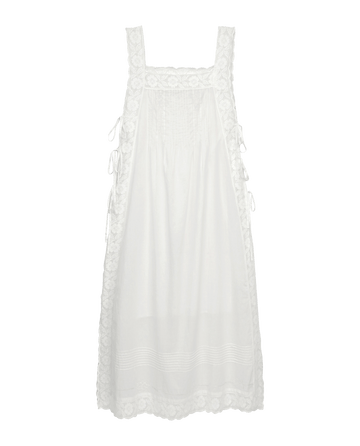 The Attic Lace Dress by THE GREAT. SU25 in white features lace trim, a square neckline, side ties, and front vertical pleats, displayed on a black background.