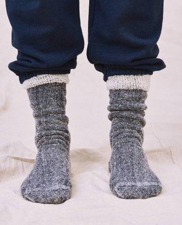Showcasing style with The Sweatshirt Sock in Navy Blue, a person pairs these with sweatpants, creating the perfect look against a light fabric surface.