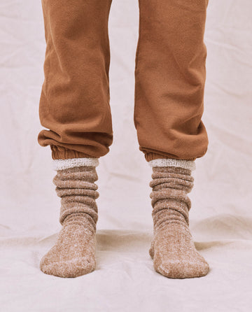 A person wearing The Sweatshirt Sock in Nutmeg stands on a white surface. Brand: THE GREAT. SP25 SWEATSHIRT SOCKS.