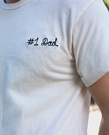 Close-up of a person wearing The Men's Boxy Crew in washed white by THE GREAT. MAN, a perfectly fitting, classic staple white cotton tee with the embroidered text "#1 Dad" on the chest.