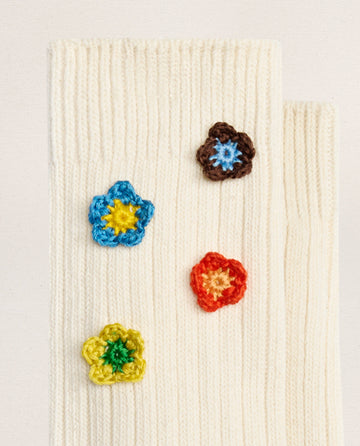 EMME’s THE CROCHET FLOWER SOCK (4 FLOWERS) in cream features hand-crocheted blue, brown, orange, and yellow flower appliqués for a vintage touch to your everyday look.