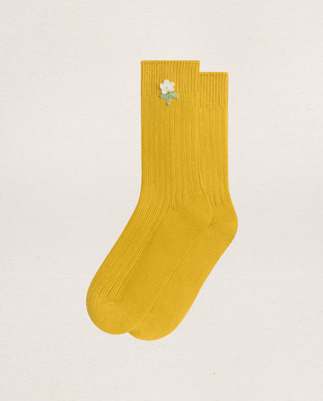 The CROCHET FLOWER SOCK (1 FLOWER) -- MARIGOLD by EMME features yellow ribbed cotton and a hand-crocheted white flower near the top, bringing vintage charm to any look.
