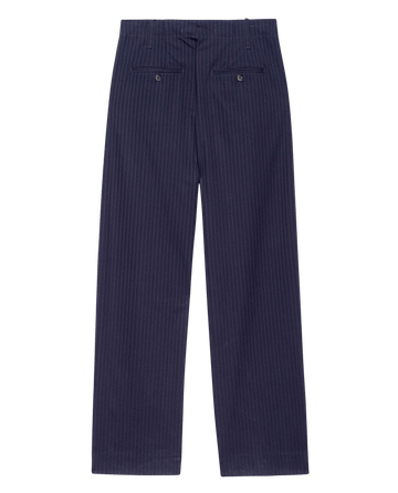 The Menswear Trouser in dark blue stripe by THE GREAT. F25 COLLECTORS features a classic straight-leg, high-rise fit with back welt pockets and button closures, shown flat on a white background.