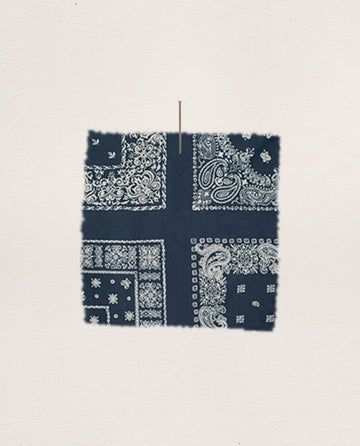 The Smocked Sleep Top in Bandana Patchwork by THE GREAT. F25 SLEEP, featuring navy blue fabric with white paisley and geometric prints, is pinned to a light beige background.