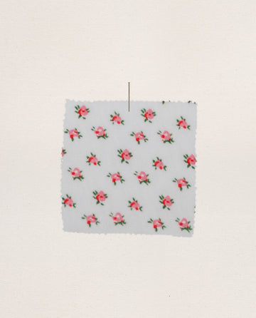 A square swatch of The Jersey Sleep Robe — Calico Rose by THE GREAT. PS26 SLEEP, featuring a white fabric with small pink rose prints, is pinned to a light background.