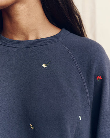 A person wearing a navy blue sweatshirt with small embroidered flowers in various colors near the shoulder and chest area.