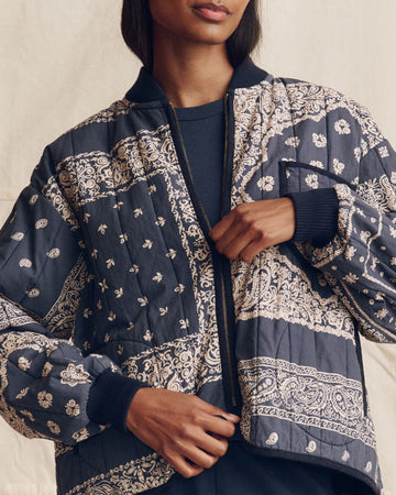 A person wearing a navy blue quilted jacket with cream-colored floral and paisley patterns zips up the front.