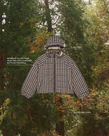 THE GREAT. F25 TGO’s Whistler Puffer in Mini Frosted Daisy, shown with trees, features plush lining, elasticated cuffs, and eco-friendly PrimaLoft Black Thermo Plume insulation made from 100% post-consumer materials.