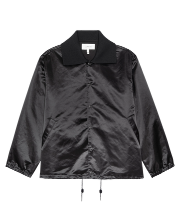 The Satin Coach's Jacket in black by THE GREAT. H25 COLLECTION, features long sleeves, button-up front, collar, angled pockets, and adjustable drawstring hem. Displayed on a plain white background.
