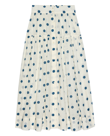 The Highland Skirt by THE GREAT. PS26 features a cream base with blue polka dots, a button-down front, gathered waist, and knee-length cut, all crafted from lightweight cotton for comfort.