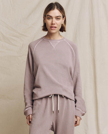 A person is wearing The Slouch Sweatshirt in Quartz by THE GREAT. HOL 24 KNITS and matching pants while standing against a beige fabric backdrop.