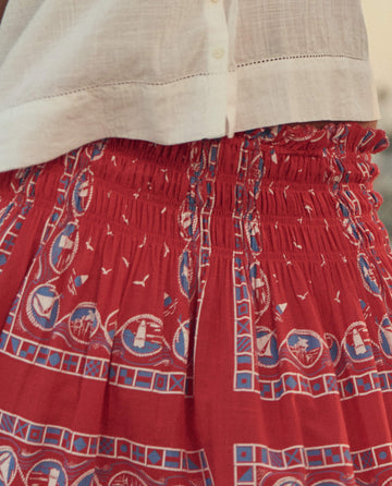Close-up of a person wearing a white shirt and THE GREAT. SU26 The Canary Skirt -- Red Sailboat Bandana, featuring a blue and white nautical sailboat and seagull pattern.