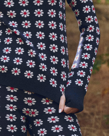 A person outdoors wears THE GREAT. F25 TGO’s The Merino Legging in Frosted Daisy, a navy blue set with white and red daisy patterns—ideal for a stylish slopeside companion look.