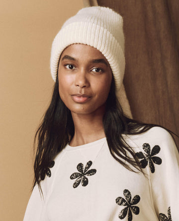 A person wearing The Natural Alpaca Beanie in cream by THE GREAT. HOL 24 BIRKENSTOCK and a floral-patterned sweater stands against a neutral background.