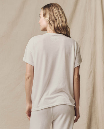 Wearing The Boxy Crew in Washed White by THE GREAT. CORE KNITS, a person with long hair stands against a beige background, facing away and styled in pants.