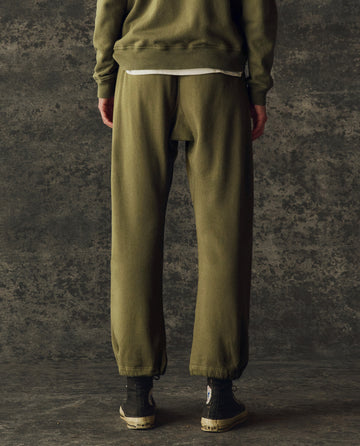 A person faces away from the camera wearing THE GREAT. H25 BRIGHT FLEECEBACK The Fleece Sport Sweatpant in Army, a matching jacket, black high-top sneakers, and a white shirt.