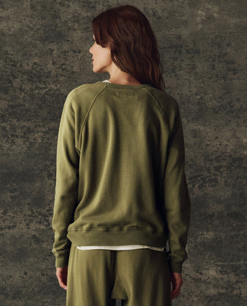 Person stands with their back to the camera in THE GREAT. H25 BRIGHT FLEECEBACK The Fleece Rookie Sweatshirt, Solid -- Army, and matching pants against a textured gray background.