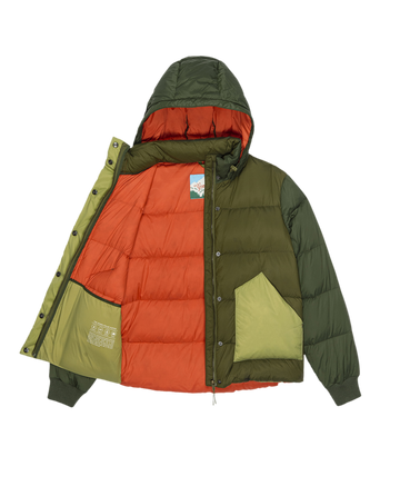 The Polar Puffer – Army Colorblock by THE GREAT. F25 TGO features olive and green panels, an orange quilted lining, front snap buttons, large pockets, and PrimaLoft Black Thermo Plume insulation for warmth.