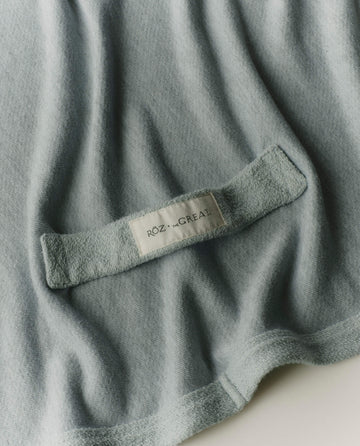 A close-up of the RŌZ + The GREAT The Sweatshirt Hair Towel in Seaglass by THE GREAT. PF25 ROZ, featuring a fabric label inside; designed for quick drying and frizz reduction.