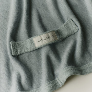 Close-up of a textured fabric with a brand label reading ROZ + THE GREAT on a light gray background