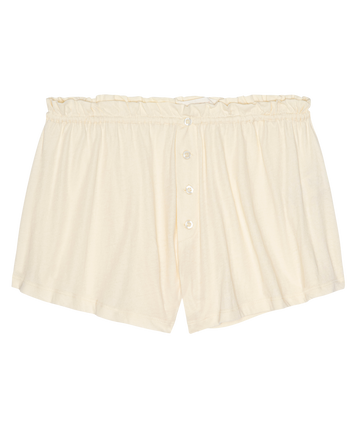 The Tap Short.. by THE GREAT. H25 SLEEP in Washed White: cream-colored women’s sleep shorts in 100% super soft cotton jersey with button front and ruffled elastic waistband, shown laid flat on a white background.