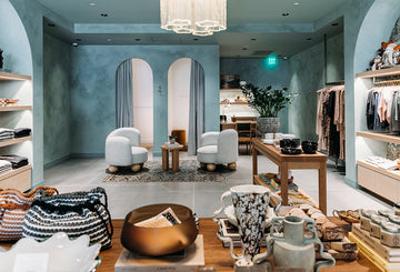 A stylish boutique with modern decor, featuring clothing racks, decorative items, and seating areas under soft lighting.