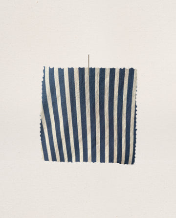 A rectangular piece of fabric from The Pajama Shirt by THE GREAT. FALL 24 SLEEP, featuring vertical blue and white Horizon Stripes reminiscent of vintage pajama tops, is pinned to a plain light background.