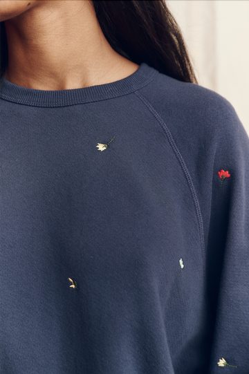Close-up of a person wearing THE GREAT. PS26 The College Sweatshirt in navy, featuring tossed floral embroidery—an oversized vintage-inspired piece ideal for cool Los Angeles days.