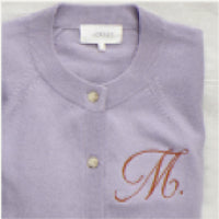 A folded light purple cardigan with beige buttons and a cursive letter "M" embroidered on the chest.