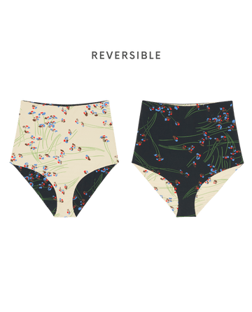 The Reversible High Rise Covered Brief by THE GREAT. SP26 SWIM is shown in Windblown Bouquet, featuring vintage-inspired floral patterns on cream and black backgrounds. Text above reads "REVERSIBLE," perfect for fans of retro 50s swimwear style.