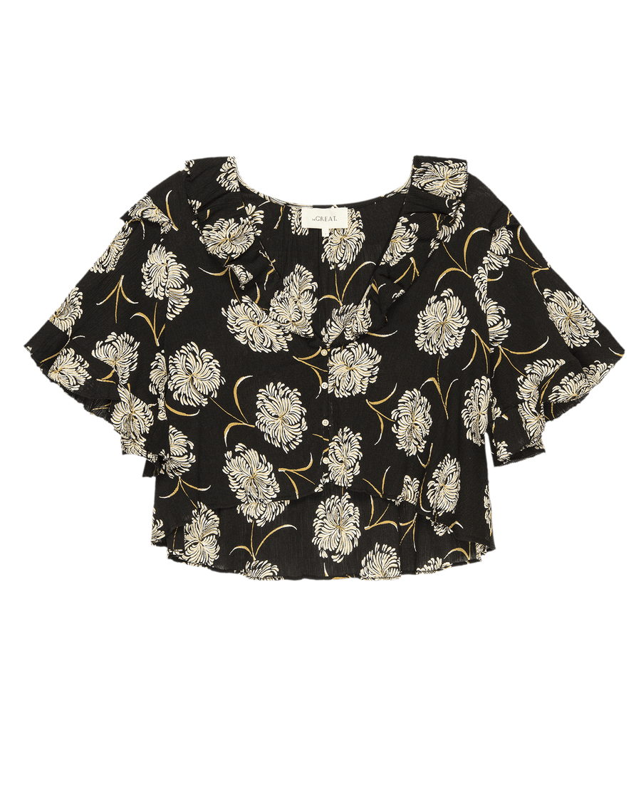 The Bower Top by THE GREAT. SU25 features a black “Dancing Floral” print, ruffled neckline, and short sleeves—a chic choice for timeless elegance, shown on a plain background.