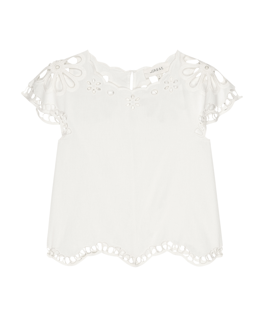 The Super Bloom Eyelet Top by THE GREAT. SU25—white short-sleeve blouse with scalloped hem and sleeves, plus floral eyelet cutouts at the neckline and edges for a fresh, feminine look.