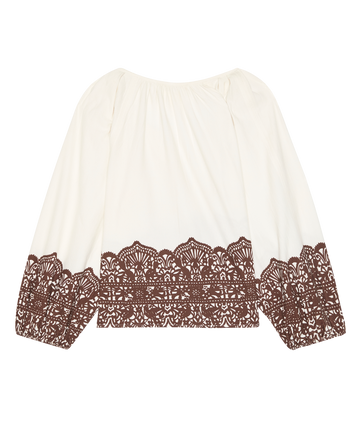The Chariot Top by THE GREAT. F25 D1 is a cream long-sleeve cotton top featuring a Western lace print along the hem and cuffs, shown laid flat on a white background.
