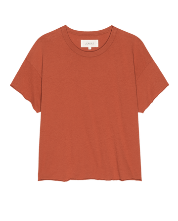 The Crop Tee. Solid -- Desert Clay by THE GREAT. SU25 SEASONAL KNITS is a rust-colored, short-sleeve crop top with a crew neckline, perfect for casual women's fashion, shown against a white background.