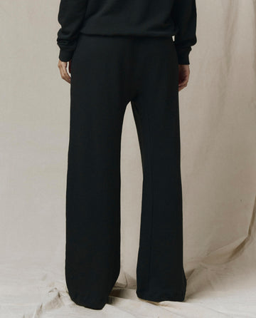 Model wearing The Horseshoe Sweatpant in Solid -- Almost Black by SP26 New Knits, paired with a black long-sleeve top, shown from the back against a neutral fabric backdrop.