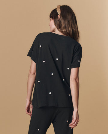 A woman with long brown hair and a tan headband models THE GREAT. PF25 EMB KNITS The Boxy Crew. Embroidered — Almost Black With Daisy Embroidery, shown from the back against a plain beige background.