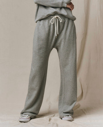 A person wears SP26 New Knits' The Horseshoe Sweatpant - Solid in Varsity Grey, featuring a relaxed fit and white drawstring, styled with white slip-on shoes against a beige fabric backdrop.