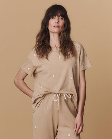 Woman wears THE GREAT. PF25 EMB KNITS The Boxy Crew. Embroidered—Khaki with Daisy Embroidery and matching pants, standing against a beige background.