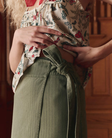 A person models THE GREAT. SP26 D1 The Wrap Skirt in Classic Army, demonstrating versatile indoor style with this timeless olive green piece.